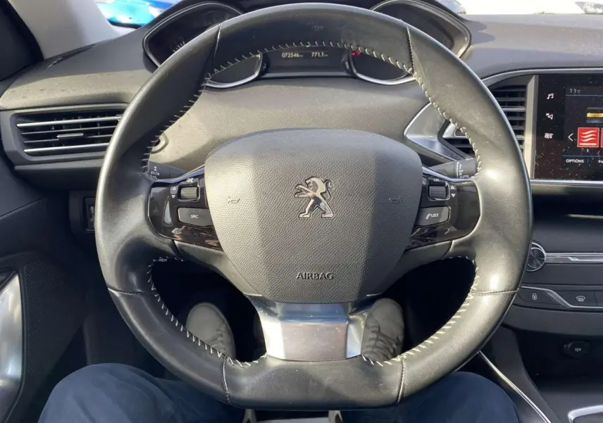 Vue centrée sur le volant cuir du Peugeot 308 blanc nacré 2017, avec tableau de bord et écran tactile visible à droite.