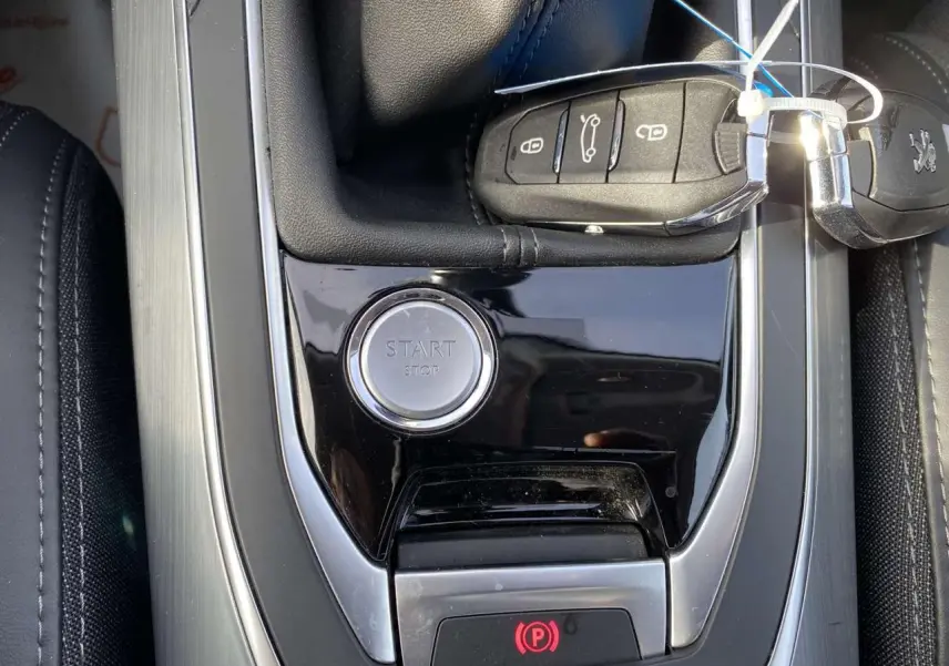 Gros plan sur la console centrale noire de la Peugeot 308 blanche avec bouton start/stop et clé électronique.