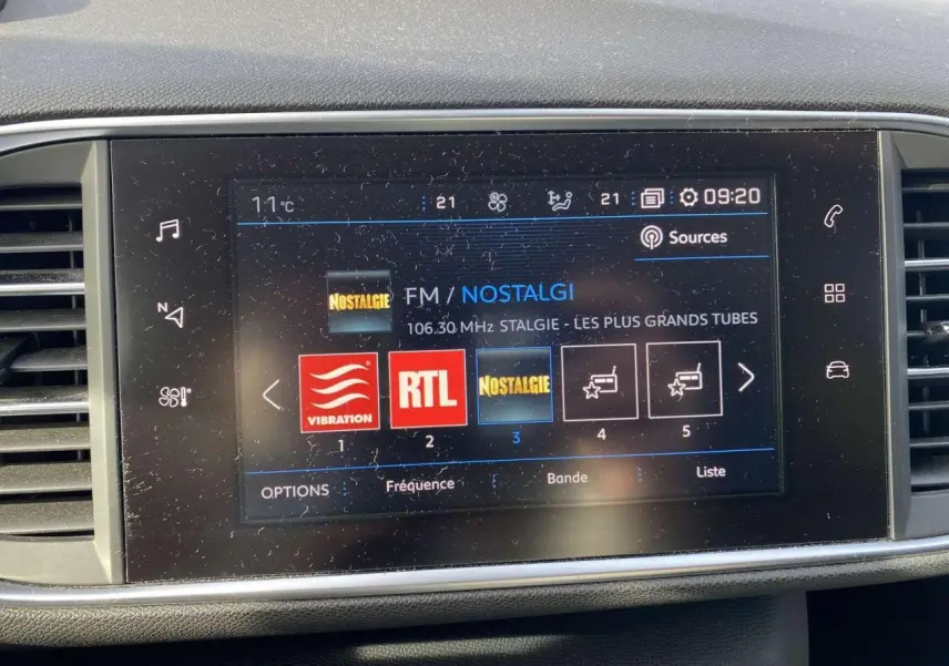 Écran tactile 9,7 pouces du tableau de bord d'une Peugeot 308 blanche, affichant les radios FM avec interface connectée.