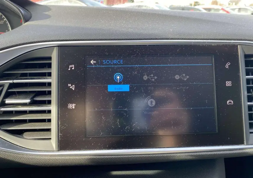 Écran tactile central allumé montrant les sources audio dans l'habitacle d'une Peugeot 308 blanche de 2017.