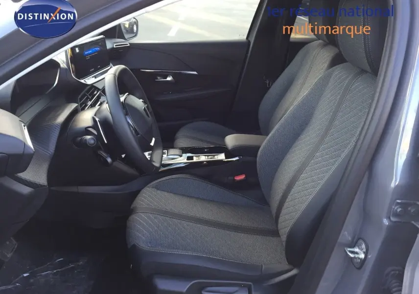 Intérieur avant droit du Peugeot 208 gris Selenium, sièges tissu noir avec console centrale et volant visible.