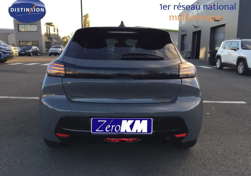 Vue arrière d'une Peugeot 208 gris selenium métal 2025 avec feux LED allumés sur parking extérieur.