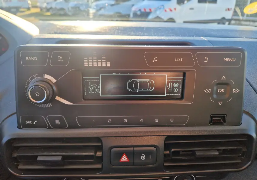 Vue rapprochée du tableau de bord du Peugeot Partner blanc 2021, affichant l’écran central avec commandes radio et climatisation.