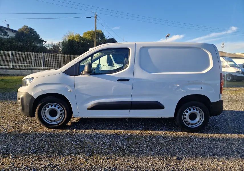 Vue de profil côté gauche d’un utilitaire Peugeot Partner blanc 2021 avec porte latérale pleine et jantes acier.