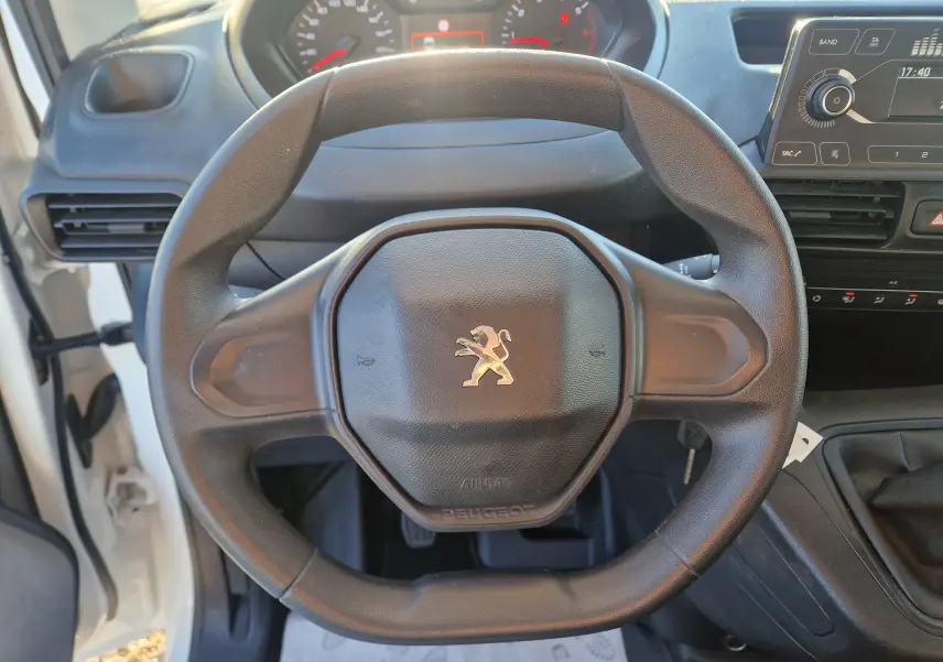 Vue rapprochée du volant noir avec logo Peugeot du Partner blanc 2021, montrant aussi le tableau de bord et la radio intégrée.
