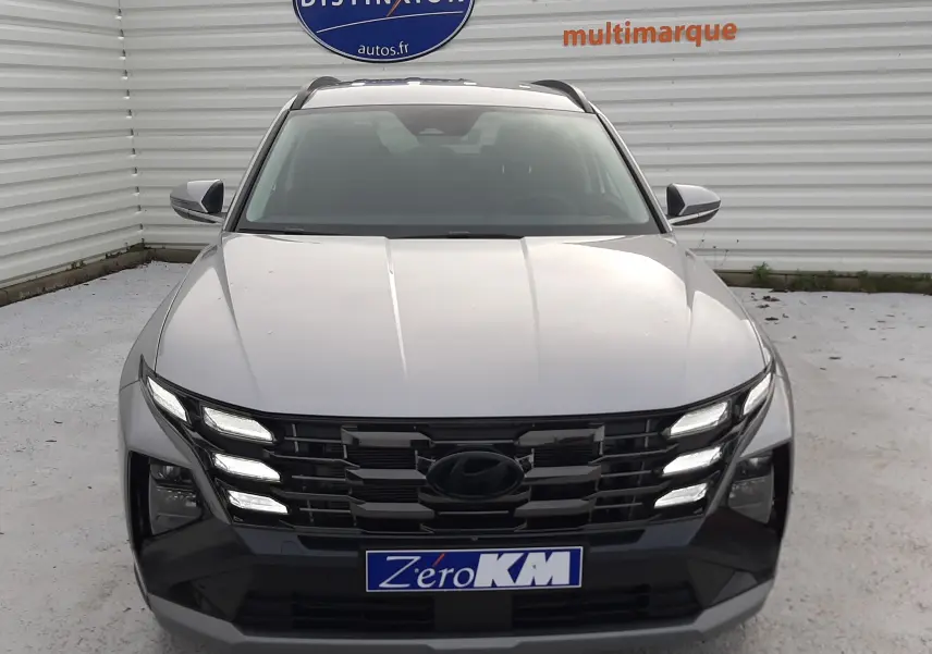 Vue frontale d'un Hyundai Tucson gris Shimmering Silver 2025 avec calandre noire et feux LED allumés.