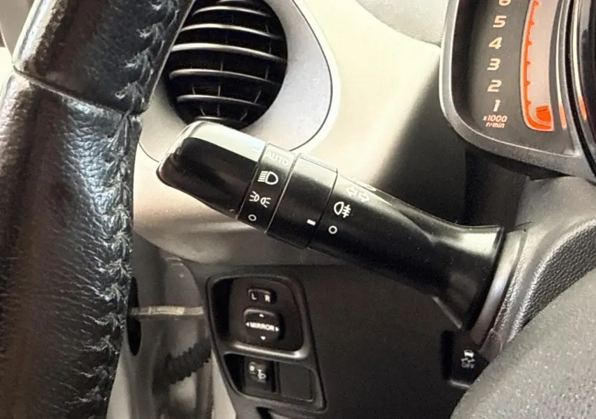 Gros plan sur la commande des phares et clignotants à gauche du volant d'une Toyota Aygo gris clair, tableau de bord partiel visible.