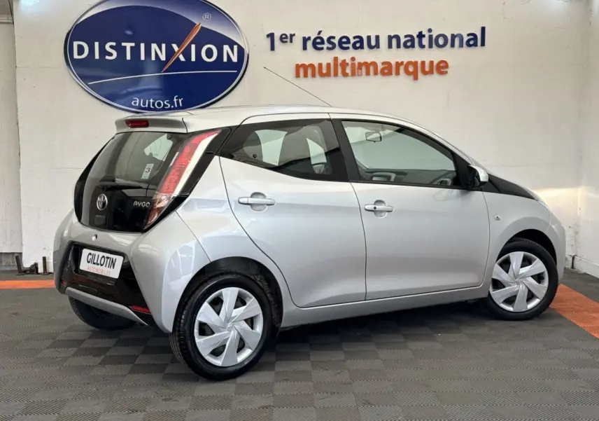 Vue 3/4 arrière droite d'une Toyota Aygo gris clair avec toit noir et feux arrière verticaux distinctifs.