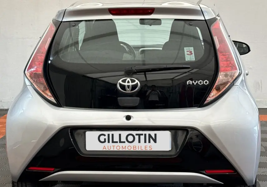 Vue arrière d'une Toyota Aygo gris clair avec hayon noir brillant et feux arrière verticaux distinctifs.