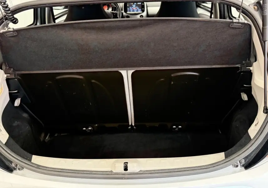 Vue du coffre arrière ouvert d'une Toyota Aygo gris clair, montrant la banquette rabattue et l'intérieur du coffre noir.