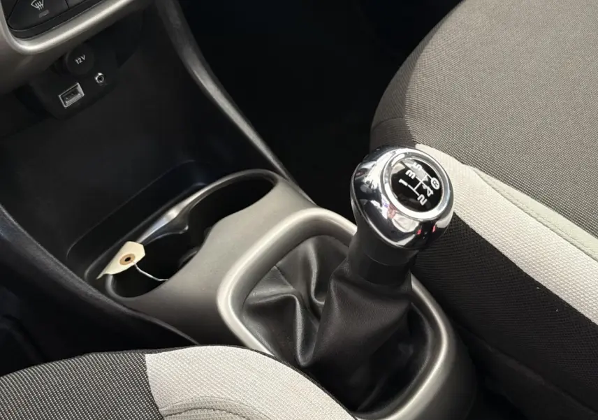 Gros plan sur le levier de vitesses manuel chromé et les sièges tissu gris clair et foncé d'une Toyota Aygo 2017.