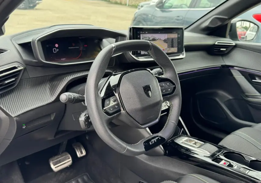 Vue intérieure du poste de conduite de la Peugeot 208 Hybrid 110 e-DCS6 GT 2025, volant GT et écran tactile visible.