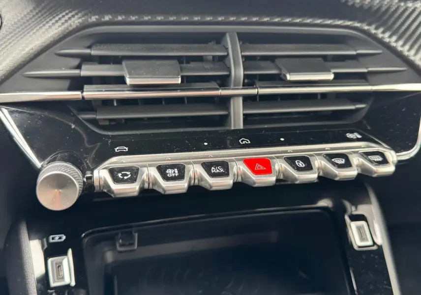 Gros plan sur la console centrale de la Peugeot 208 Hybrid 110 e-DCS6 GT 2025, boutons argentés et écran tactile noir.
