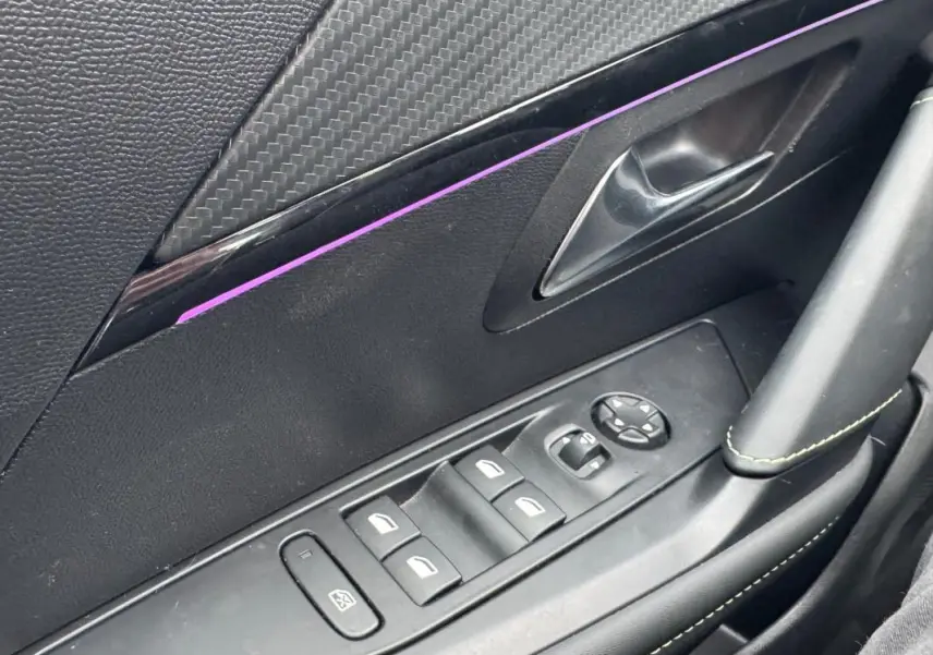 Gros plan sur la porte côté gauche de la Peugeot 208 Hybrid 110 e-DCS6 GT 2025 gris, avec commandes électriques et insert décoratif.