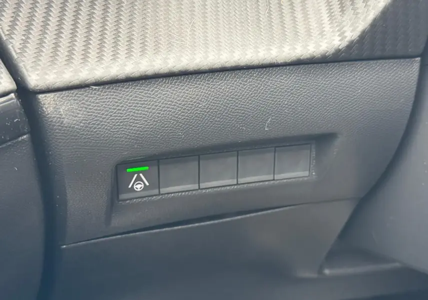 Gros plan sur le tableau de bord noir du Peugeot 208 Hybrid 110 e-DCS6 GT, montrant un bouton d’aide à la conduite activé.