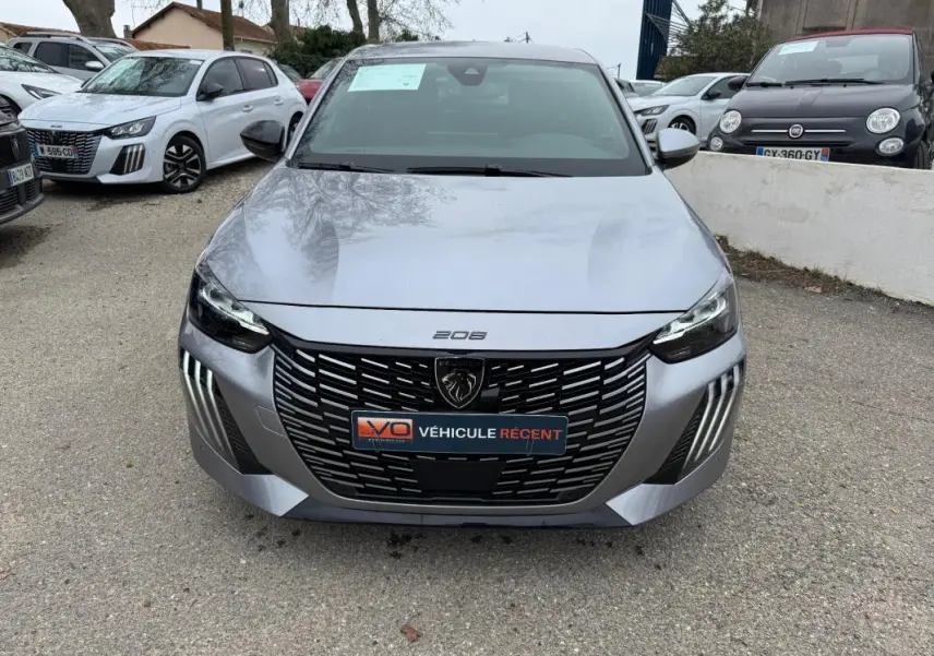 Vue frontale d'une Peugeot 208 gris clair 2025 avec calandre noire et feux LED distinctifs allumés.