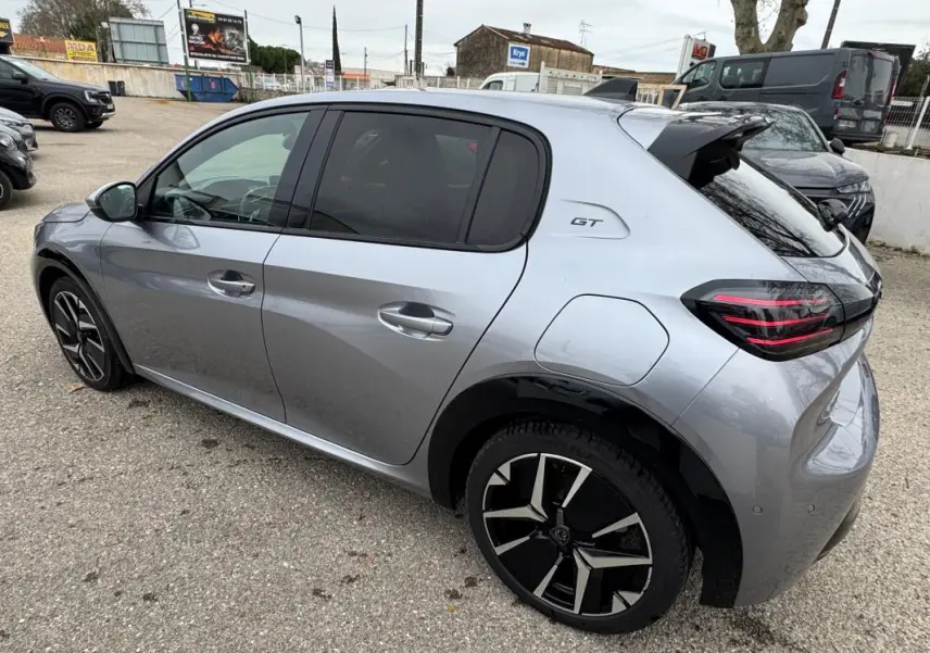 Vue 3/4 arrière droite d'une Peugeot 208 Hybrid 110 GT gris métallisé avec jantes alliage 17 pouces et logo GT sur l'aile.