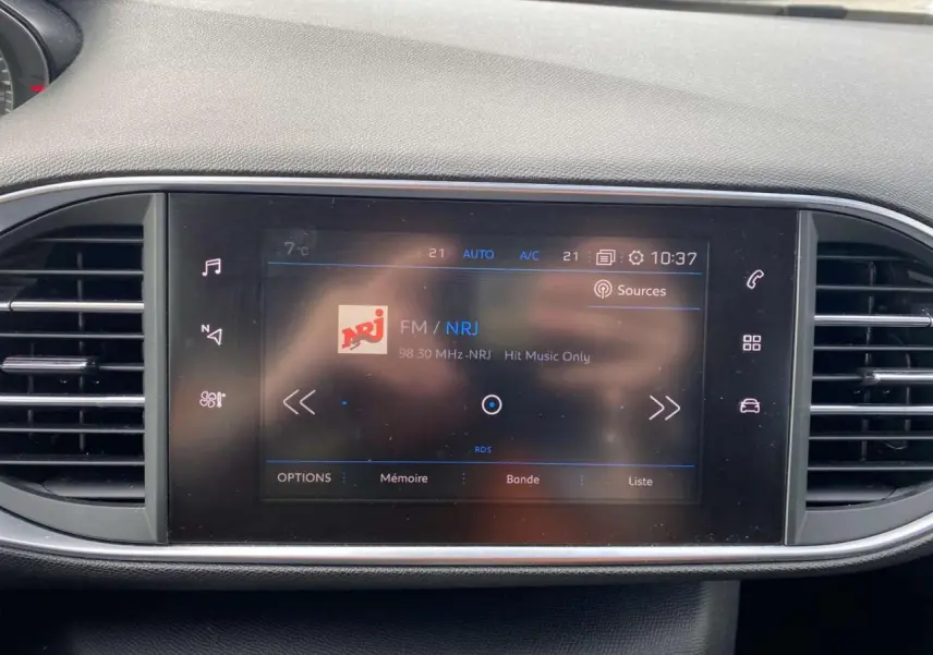 Écran tactile central du tableau de bord de la Peugeot 308 2018 affichant la radio FM NRJ, entouré de grilles d'aération noires.