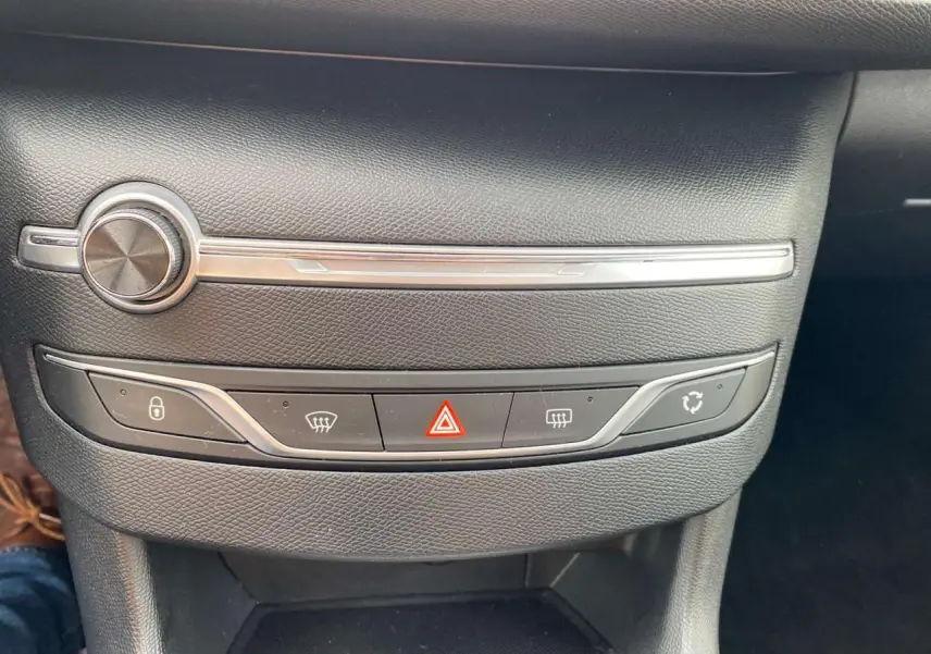 Détail du tableau de bord noir de la Peugeot 308 2018, montrant les commandes des feux de détresse et de la climatisation.