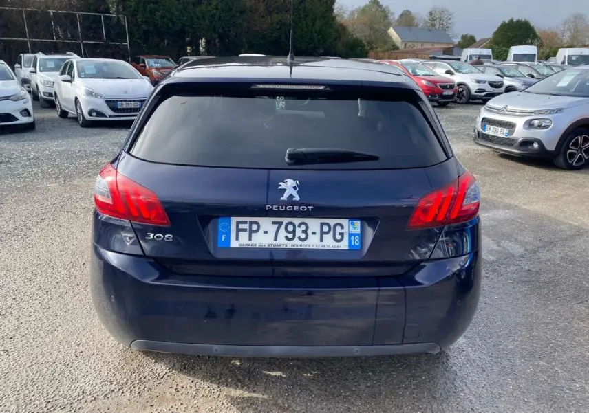 Vue arrière d'une Peugeot 308 bleu foncé avec feux arrière allumés et plaque d'immatriculation française visible.