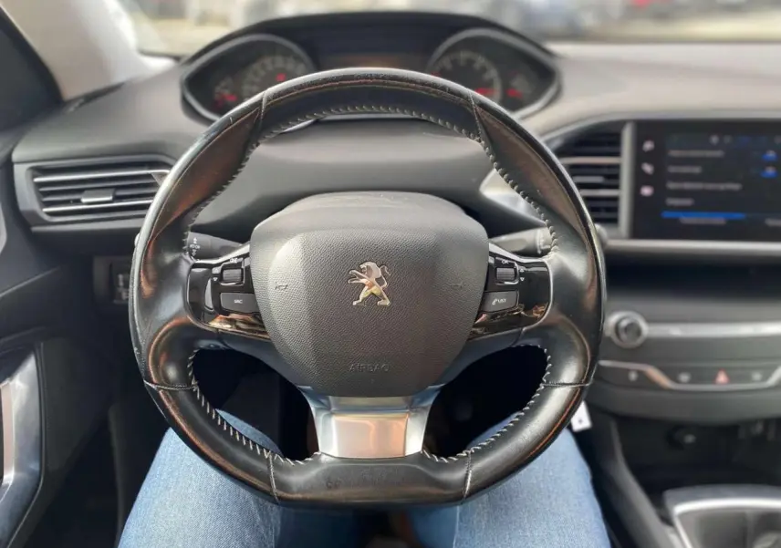 Volant en cuir noir avec logo Peugeot au centre, tableau de bord et écran tactile de la 308 style 2018 visible en arrière-plan