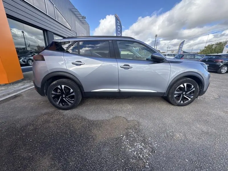 Profil droit d'un Peugeot 2008 2020 gris Artense avec toit noir, jantes alliage bicolores et barres de toit noir brillant.