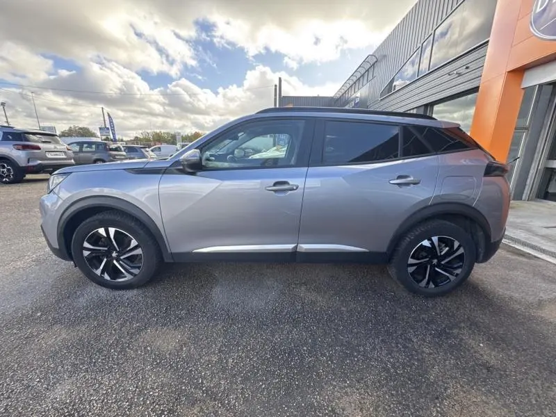 Profil droit d'un Peugeot 2008 2020 gris Artense avec toit noir et jantes alliage bi-ton, stationné devant un bâtiment.