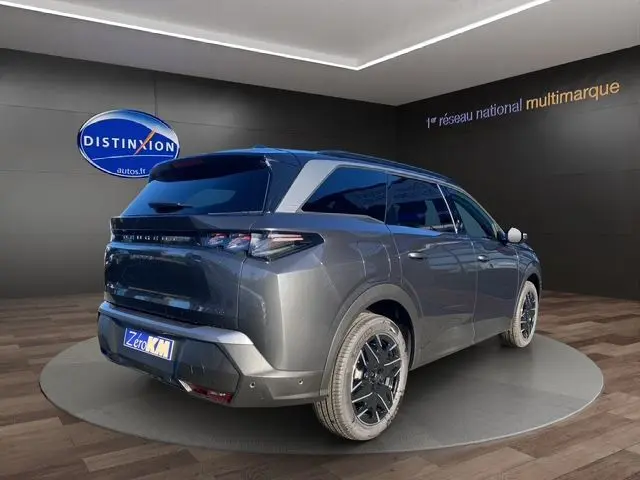 Vue 3/4 arrière droite d’un Peugeot 5008 Hybrid gris titane avec jantes noires et toit noir en showroom.