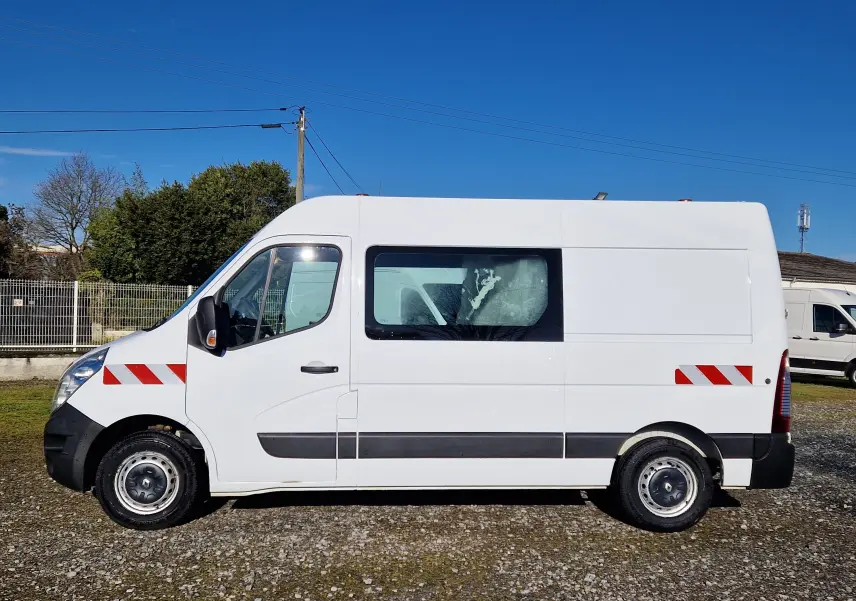 Vue latérale droite d’un Renault Master blanc avec marquages rouges réfléchissants et fenêtre latérale sur fond extérieur ensoleillé.