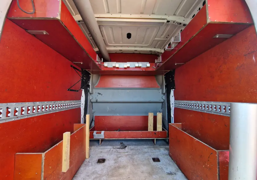 Vue intérieure arrière du Renault Master cabine approfondie blanc, montrant l'aménagement bois rouge avec rangements et étagères.