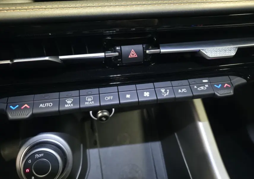 Gros plan sur la console centrale de l'Alfa Romeo Tonale gris, montrant les commandes de climatisation et le bouton de sélection de mode de conduite.