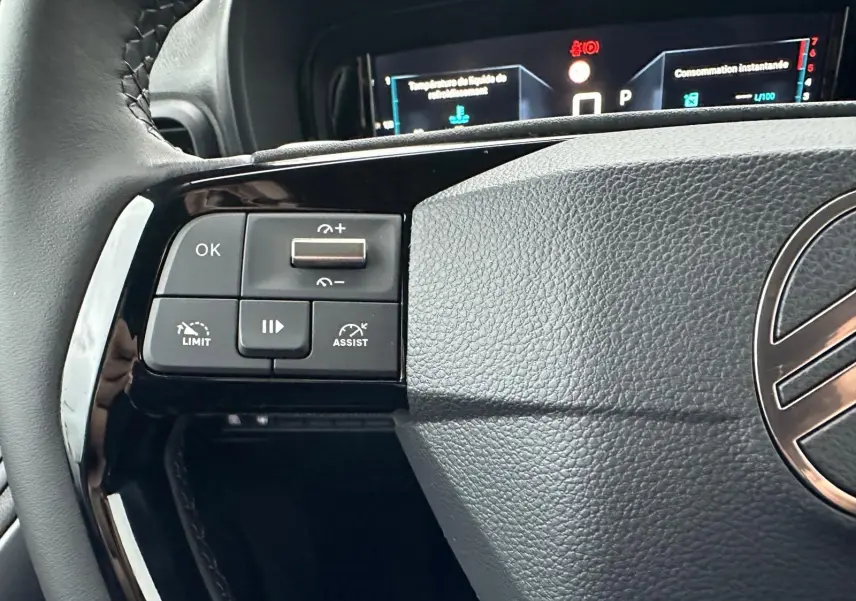 Gros plan sur les commandes à gauche du volant en cuir du Citroën Berlingo 2025, affichage numérique en arrière-plan.