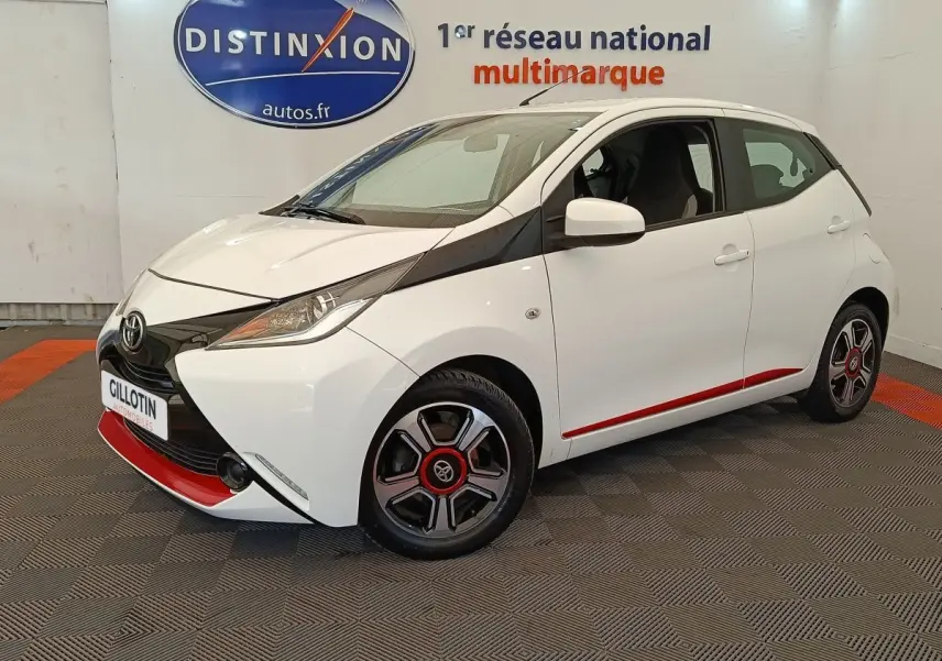Vue 3/4 avant droite d'une Toyota Aygo blanche avec détails noirs et rouges, jantes stylisées et phares ellipsoïdaux.