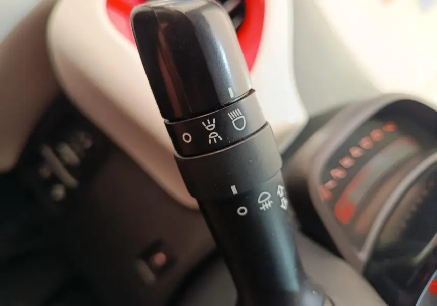 Gros plan sur la commande des phares dans l’habitacle blanc et rouge d’une Toyota Aygo 2016.