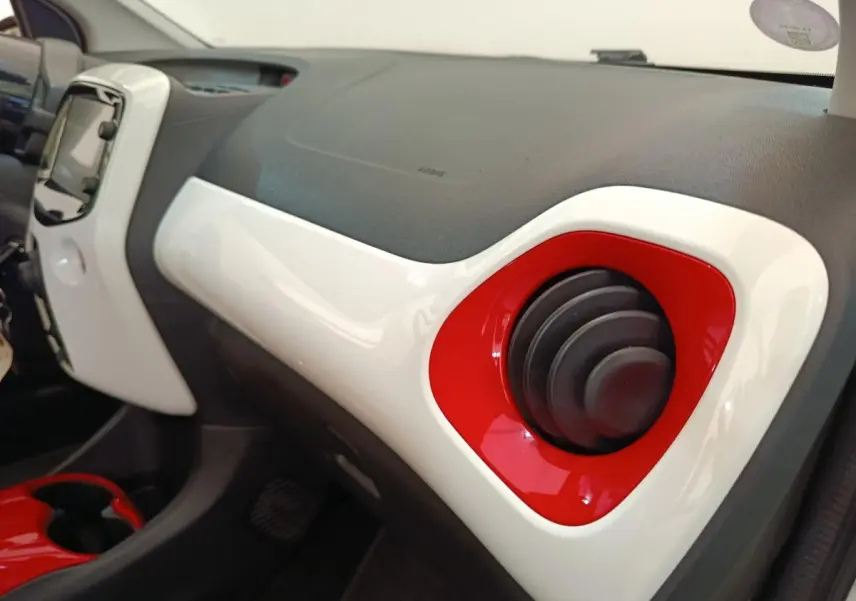 Détail intérieur du tableau de bord blanc et rouge de la Toyota Aygo 2016, avec aérateur rond rouge côté passager.