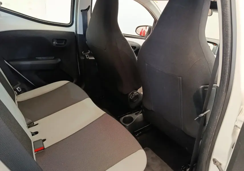 Vue intérieure arrière droite de la Toyota Aygo blanche, montrant la banquette bicolore et les dossiers des sièges avant noirs.