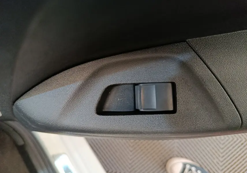 Gros plan sur l'interrupteur de verrouillage des portes côté conducteur d'une Toyota Aygo blanche, intérieur noir.