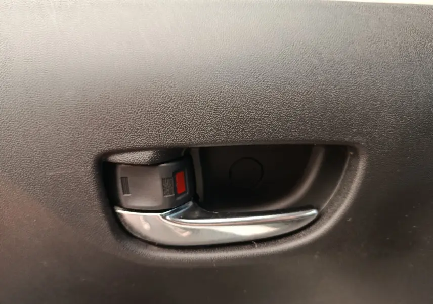 Poignée intérieure de porte avant en plastique noir et chrome sur Toyota Aygo blanc, vue rapprochée.