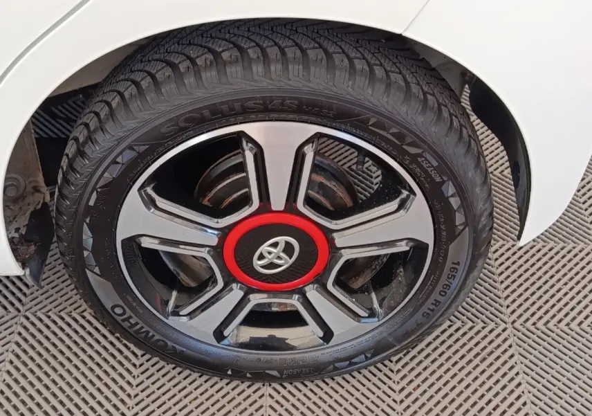 Gros plan sur la roue arrière droite d'une Toyota Aygo blanche avec jante noire et rouge distinctive.