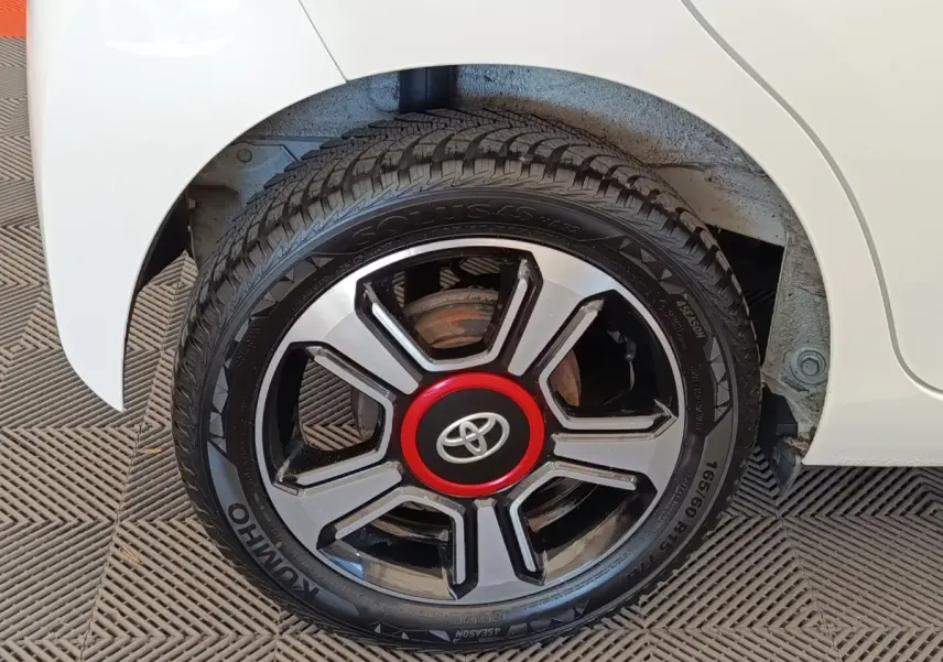 Gros plan sur la roue arrière droite blanche d’une Toyota Aygo 2016 avec jante noire et rouge distinctive.
