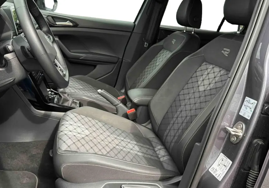 Vue intérieure côté droit sur les sièges avant gris à motif losange du Volkswagen T-Cross 2025 avec volant et levier de vitesse visibles.