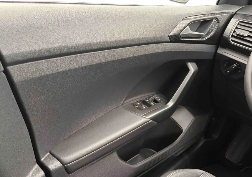 Vue intérieure côté conducteur du Volkswagen T-Cross gris, montrant la portière avec commandes des vitres et rétroviseurs.
