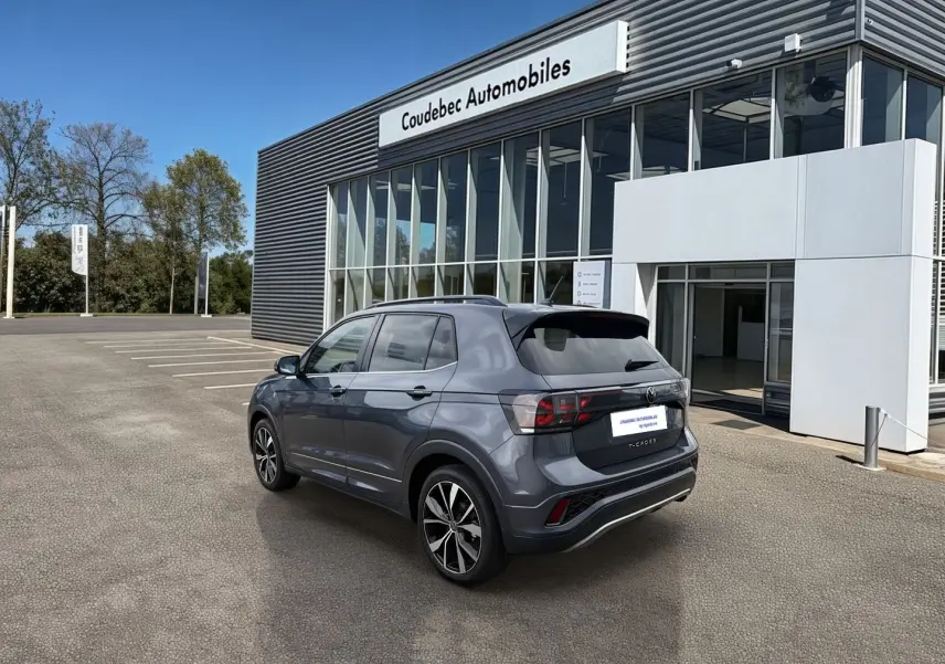 Volkswagen T-Cross gris vue 3/4 arrière droit, jantes alliage 18 pouces, stationné devant un concessionnaire.