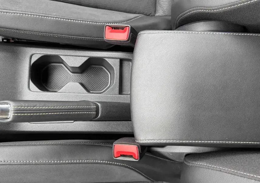 Vue rapprochée de la console centrale grise du Volkswagen T-Cross avec accoudoir, frein à main et ceintures rouges.