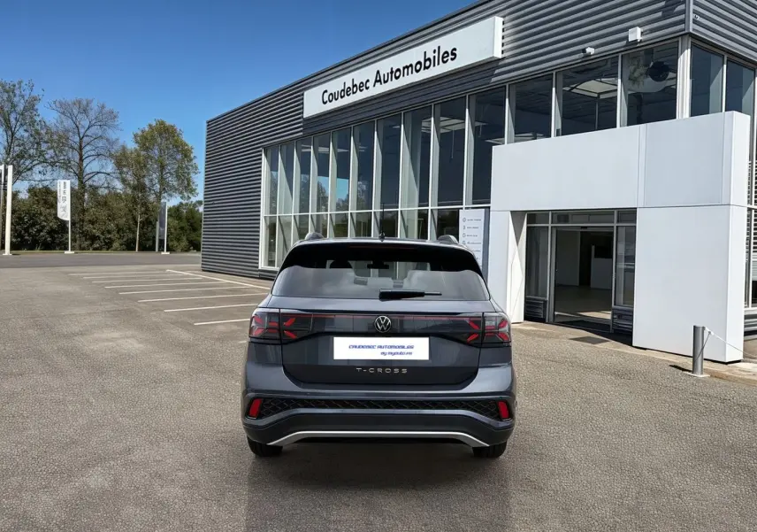 Vue arrière d'un Volkswagen T-Cross gris 2025 avec feux LED et pare-chocs R-Line devant un concessionnaire.