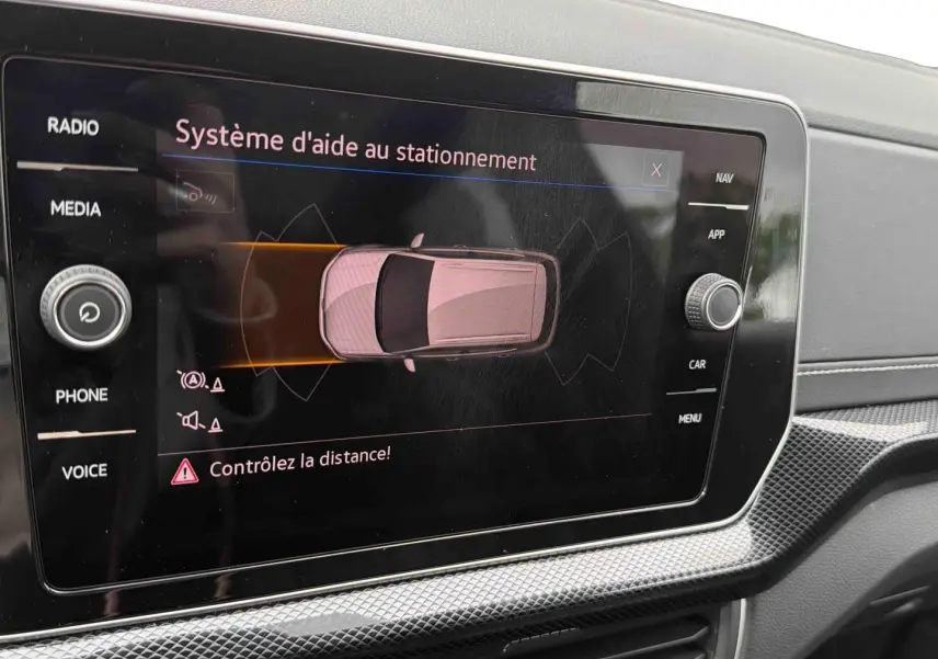 Écran tactile intérieur montrant le système d'aide au stationnement du Volkswagen T-Cross gris, vue rapprochée du tableau de bord.