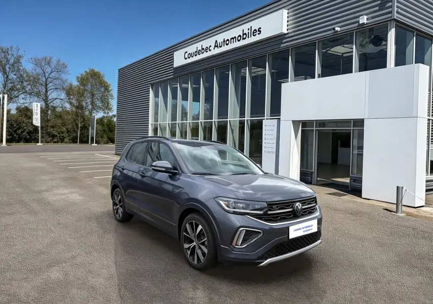 Vue 3/4 avant droite du Volkswagen T-Cross gris avec jantes alliage 18 pouces devant un concessionnaire.