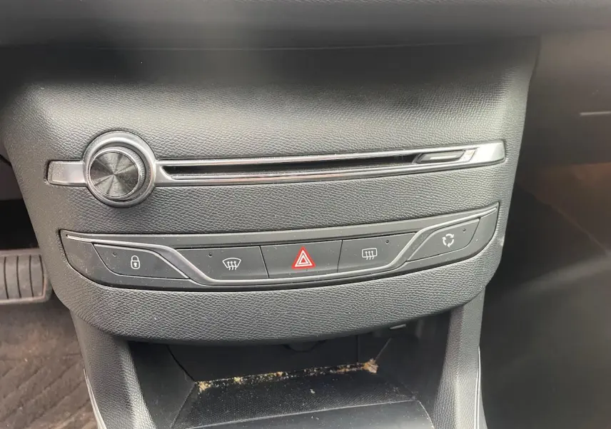 Gros plan sur la console centrale noire de la Peugeot 308 gris Hurricane, avec commandes de climatisation et bouton hazard.