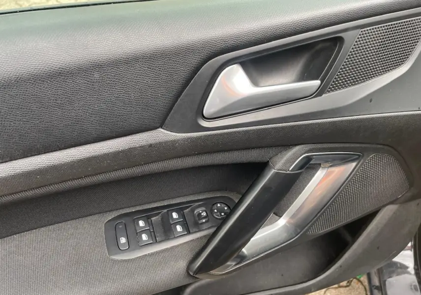 Intérieur côté gauche de la porte d’une Peugeot 308 gris Hurricane, avec commandes de vitres et poignée argentée.