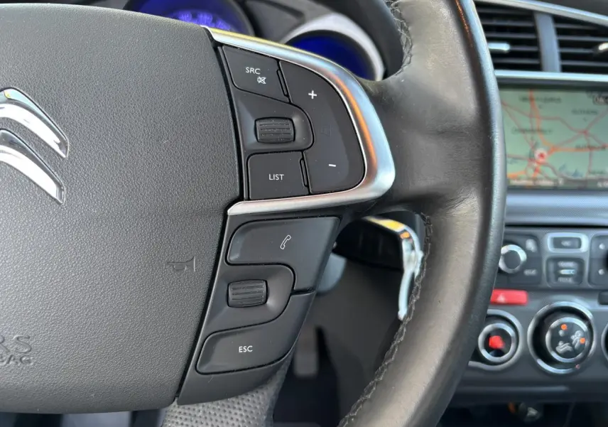Gros plan sur le volant noir de la Citroën C4 2012 avec commandes intégrées et écran de navigation en arrière-plan.